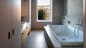 A modern bathroom with a large bathtub, a window with a view of buildings, and a wooden vanity. - Sublime 4BD House W/park Views - London Fields! (London)