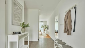 Un couloir avec une console blanche, une plante en pot et un porte-manteau sur lequel est accrochée une veste.