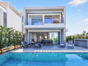 Una casa moderna de dos pisos con piscina, mobiliario exterior y una pérgola.