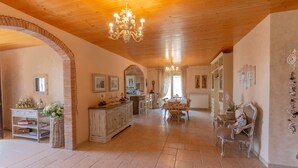 Amplia habitación con techo de madera, una araña, zona de comedor con mesa y sillas, y un aparador decorativo.