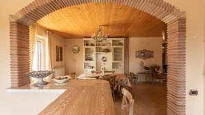 Un comedor con una mesa y sillas de madera, una araña y un aparador con puertas de vidrio.
