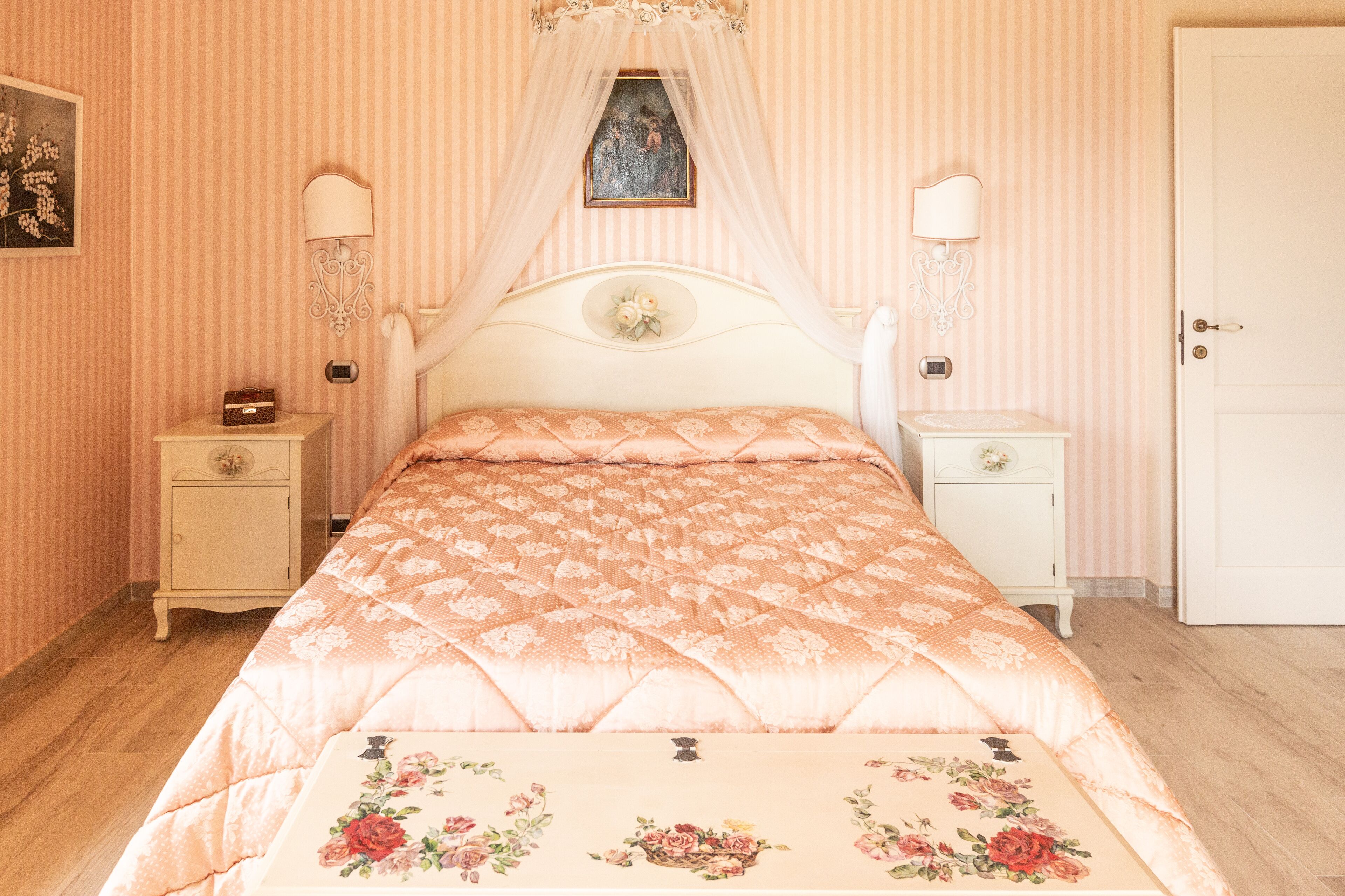 A bedroom with a bed, two bedside tables, a nightstand, a door, and a wall-mounted lamp.
