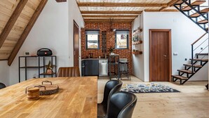 Un espacio habitable estilo loft con vigas de madera expuestas, pared de ladrillo, una zona de cocina y una escalera.