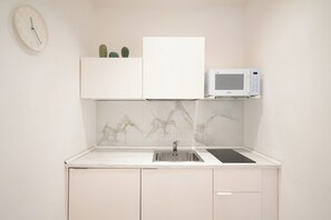 A compact kitchen with a white microwave, a sink, and a backsplash with a marble pattern.
