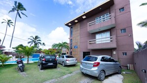 A multi-story building with a pool, parked cars, and palm trees. - HOTEL POUSADA WS  (Ipojuca)