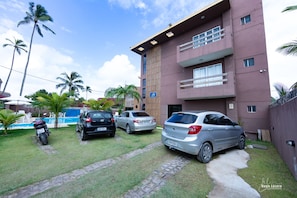 Un edificio de varios pisos con piscina, coches aparcados y palmeras.