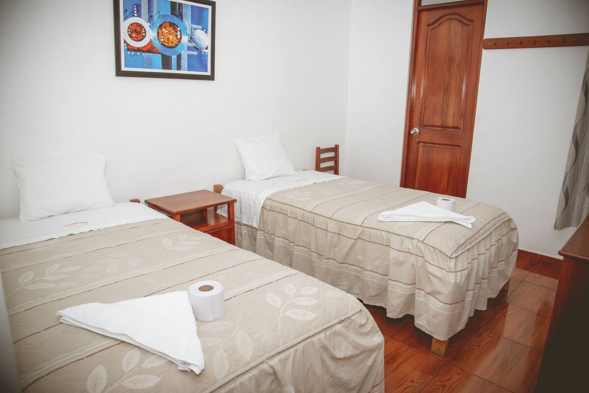 Une chambre d’hôtel avec deux lits, une porte en bois, une petite table et un tableau au mur.