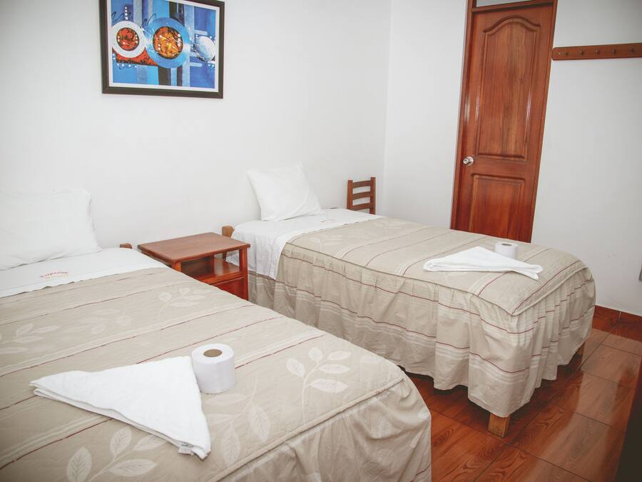 A hotel room with two beds, a wooden door, a small table, and a painting on the wall.
