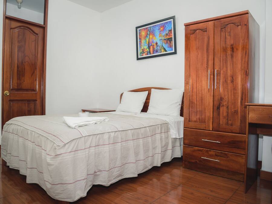 A bedroom with a bed, wooden wardrobe, and a painting on the wall.
