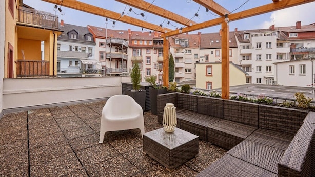 A rooftop terrace with a wooden pergola, seating area, and potted plants.
