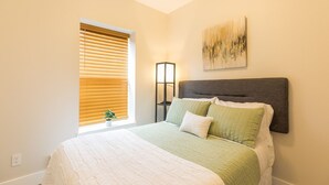A bedroom with a bed, a nightstand, a lamp, and a window with blinds. - Updated 2 Bedroom Apartment (Great Falls)