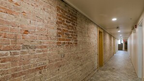 A hallway with exposed brick walls, a tiled floor, and doors leading to rooms. - Updated 2 Bedroom Apartment (Great Falls)