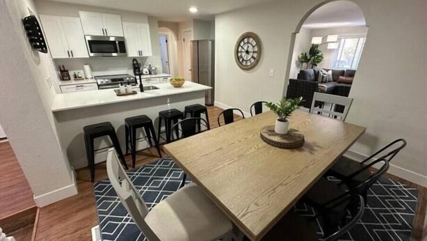 A modern kitchen with white cabinets, a central island, and a dining area with a wooden table and bar stools. - Cozy Mountain Escape (Taylorsville)