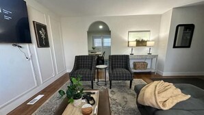 A living room with a flat-screen TV, two plaid armchairs, a coffee table with a tray, a grey sofa, and a fireplace with a lamp. - Cozy Mountain Escape (Taylorsville)