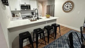 A modern kitchen with white cabinets, a microwave, a sink, and a large island with stools. - Cozy Mountain Escape (Taylorsville)