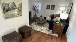 A living room with a sofa, coffee table, and ottoman, a fireplace, and a painting on the wall. - Cozy Mountain Escape (Taylorsville)