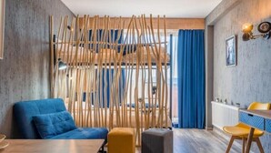 A modern room with a blue sofa, a wooden partition, a yellow chair, and a dining table.