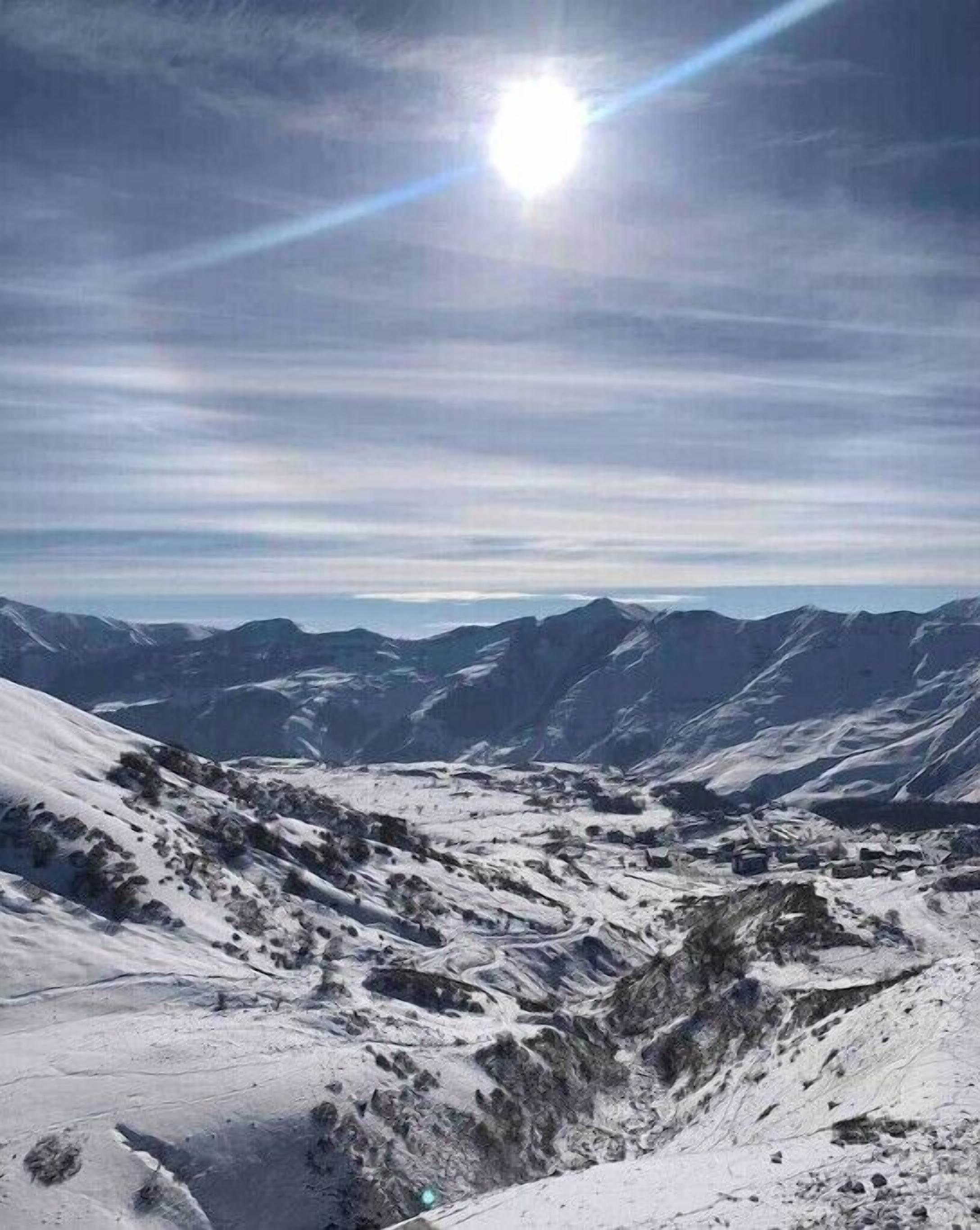Paisaje montañoso nevado con cielo despejado y montañas a lo lejos.