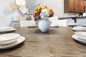 A dining table with a white vase of flowers, surrounded by white plates and bowls.