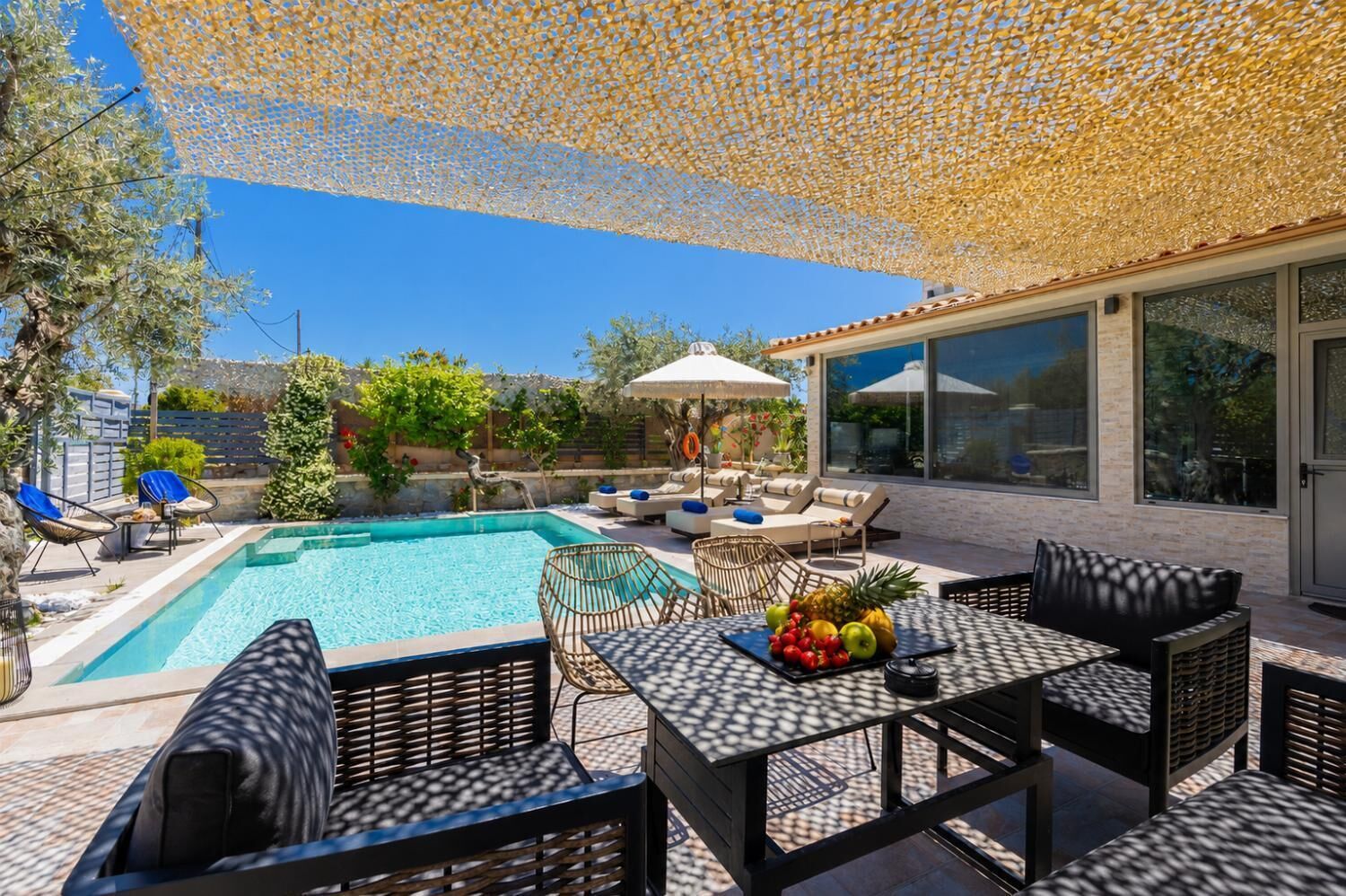 A poolside area with a pool, lounge chairs, a table with fruit, and a covered seating area.