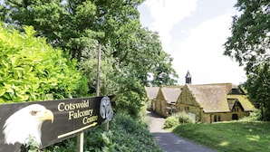 Placa para o Centro de Falcoaria de Cotswold, com um caminho que leva a edifícios de pedra tradicional.