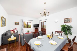 Un coin repas avec une table dressée pour quatre personnes, un canapé gris, un téléviseur et une plante.