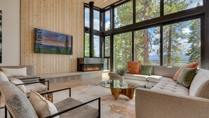 A modern living room with a fireplace, large windows, and a view of trees. - Boulder Place Lookout At Northstar - TLUXP (Truckee)