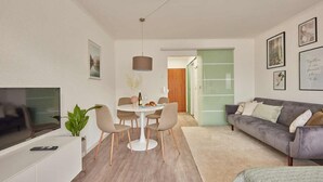 A modern living room with a flat-screen TV, a dining table with chairs, a grey sofa, and a green door in the background. - Baiersbronn - Bärbel, im Schwarzwald-stil (Baiersbronn)
