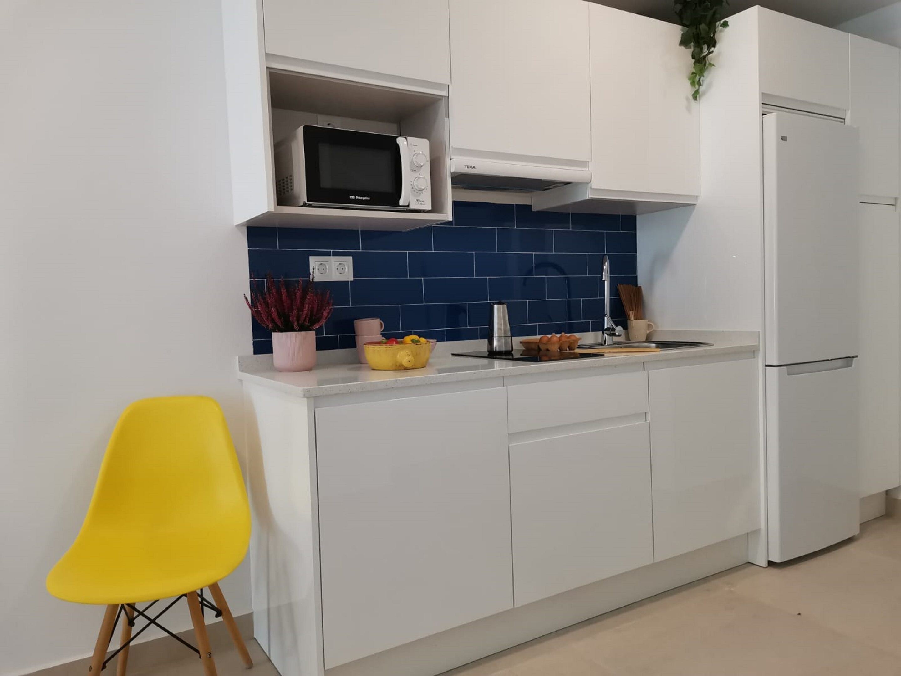 Une cuisine moderne avec des meubles blancs, un four à micro-ondes, un évier et une chaise jaune.