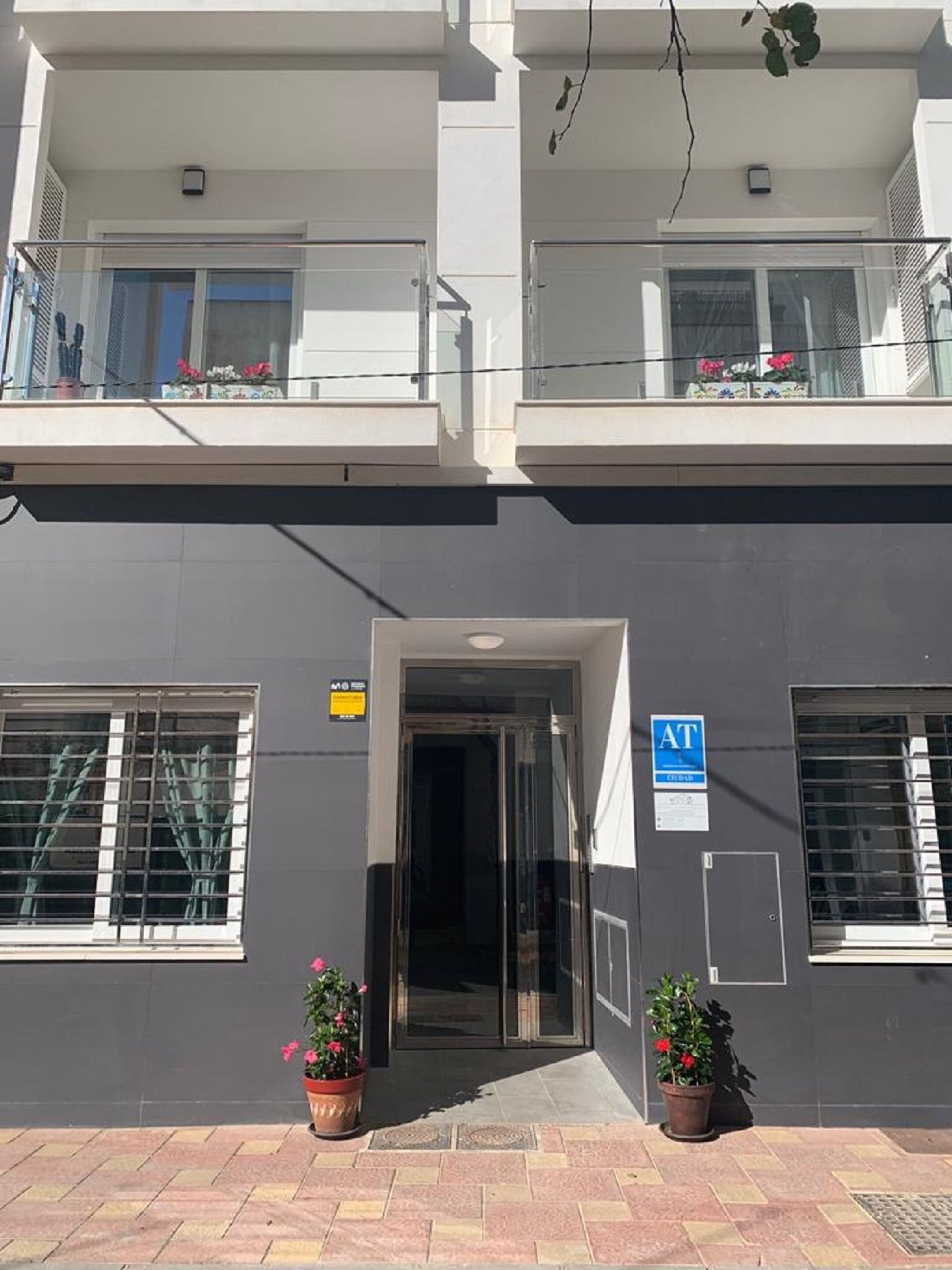 A two-story building with a dark facade, a glass entrance, and potted plants on the ground floor.