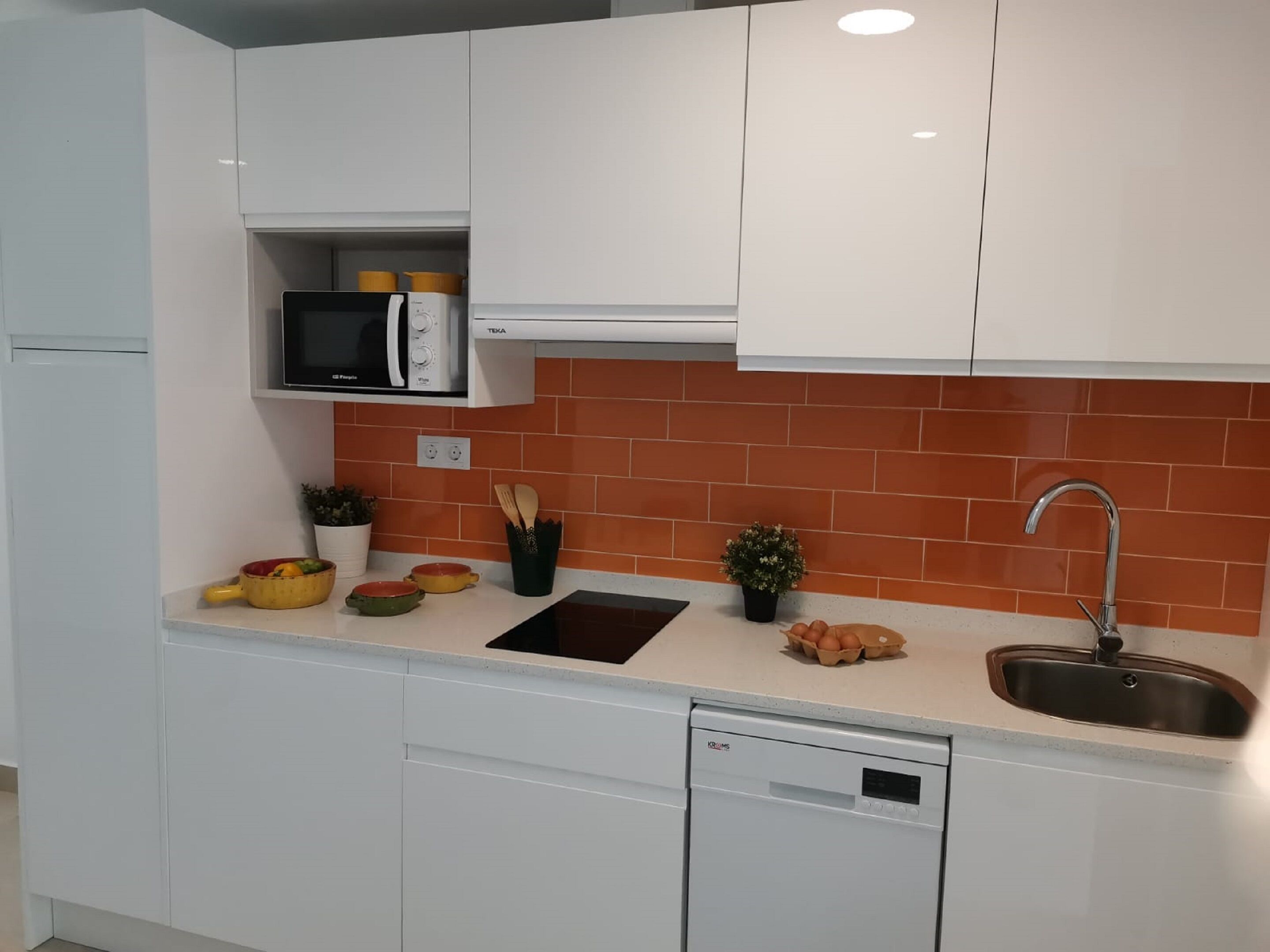 Una cocina moderna con armarios blancos, un microondas, un fregadero y un lavavajillas.