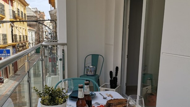 A balcony table set with dinnerware, bottles, a plant, and a wine glass. - BNBOOK MEDEA APARTMENTS 2 (Fuengirola)