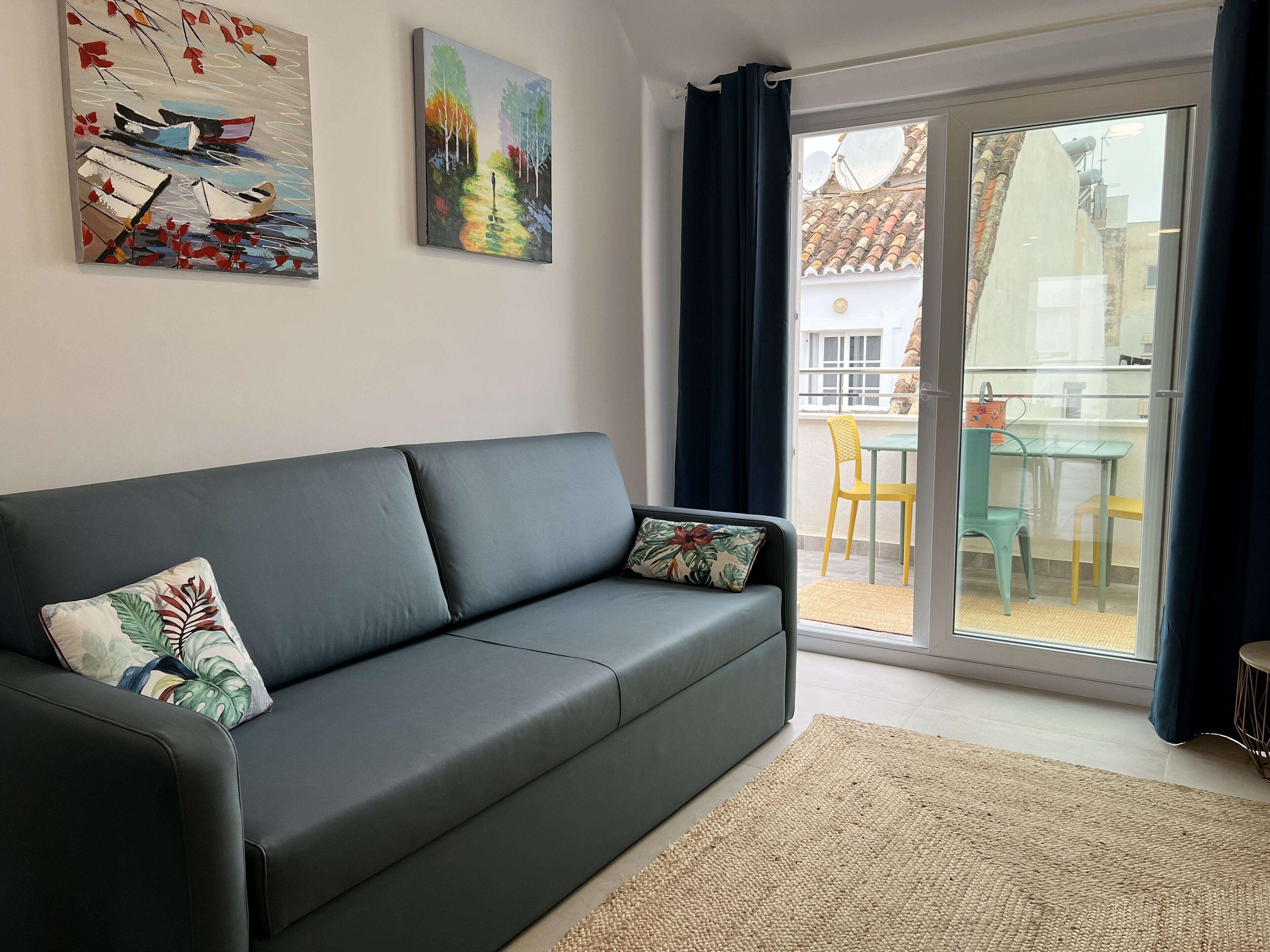A modern living room with a grey sofa, a woven rug, and two artworks on the wall.