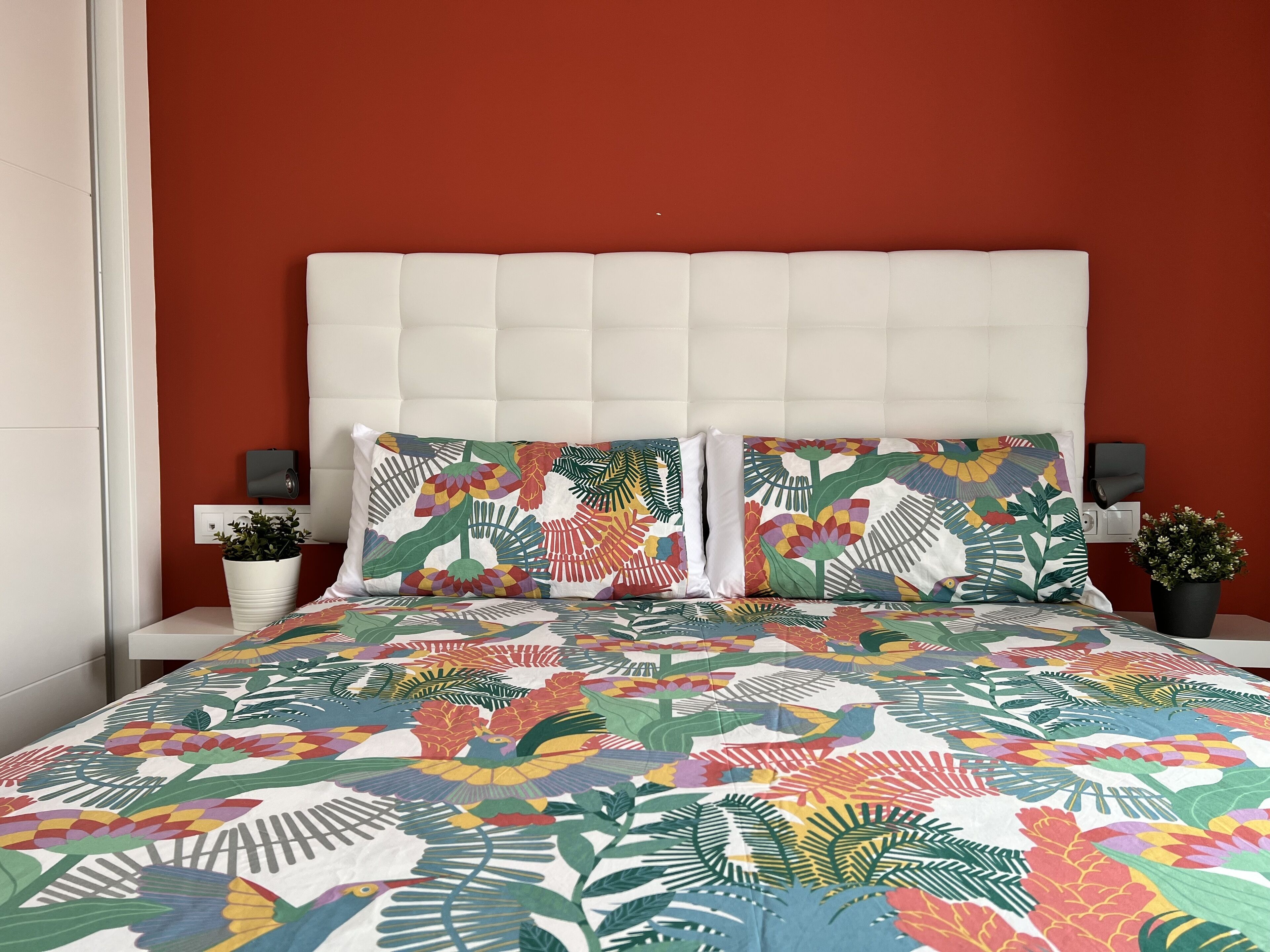 A bed with a colorful floral bedspread, a white headboard, and two nightstands with small potted plants.