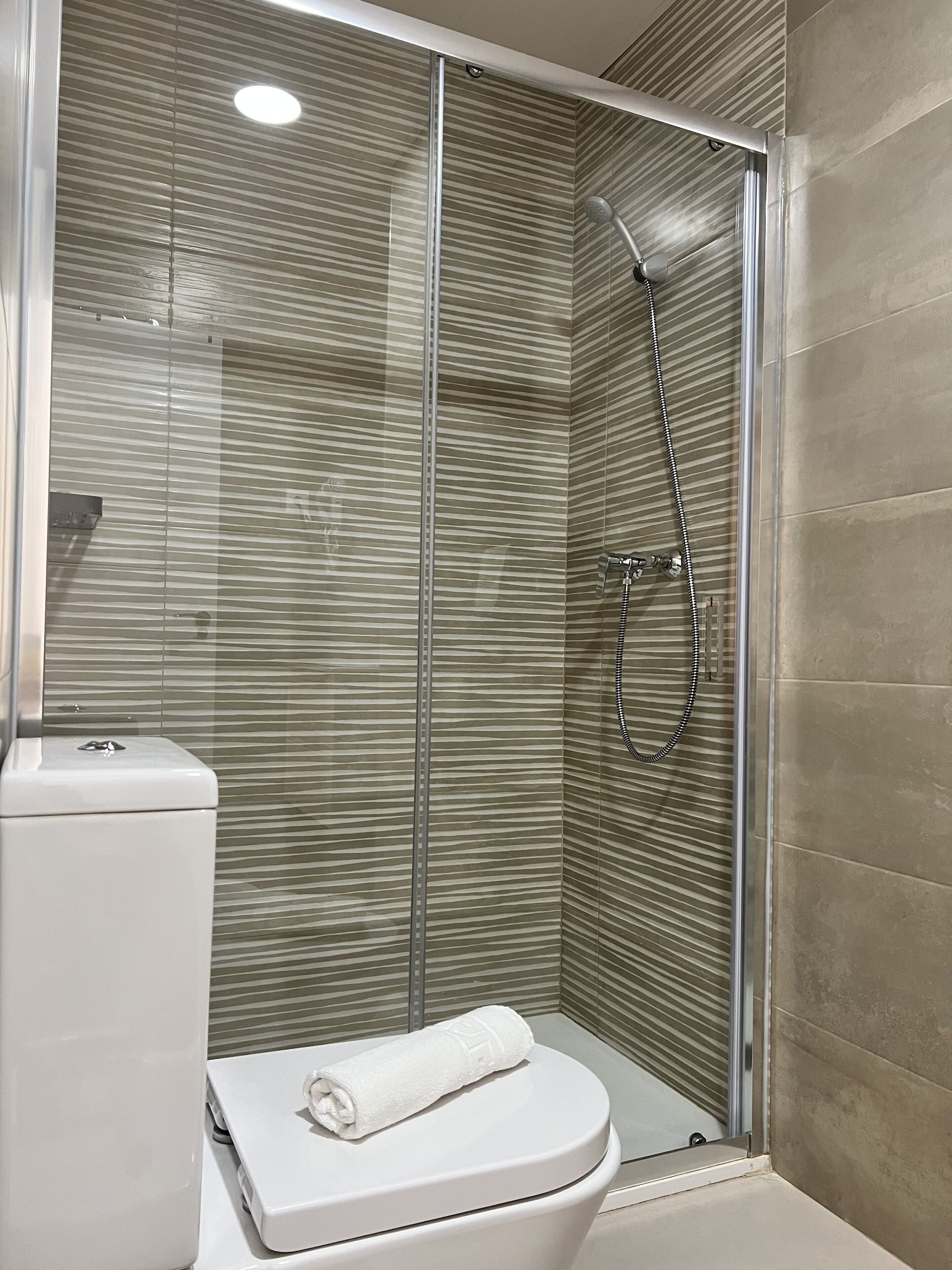 A modern bathroom with a glass-enclosed shower, a toilet, and a towel on the toilet seat.