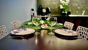A dining table set with two plates, two wine glasses, and a centerpiece of flowers. - Moehani Beach Lodge (Puna'auia)