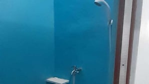 Un espacio de ducha pequeño y cerrado, con una pared azul, un estante blanco y un balde en el suelo.