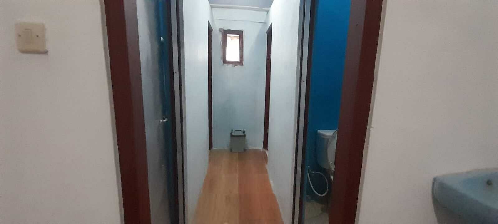 A narrow hallway with wooden flooring, a small window, and a blue wall.