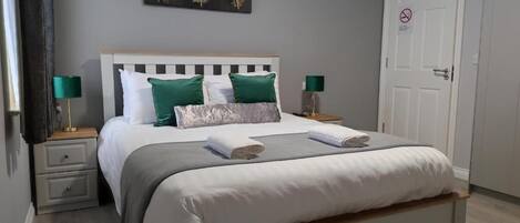 A neatly made bed with white and green bedding, a headboard, and two bedside lamps.