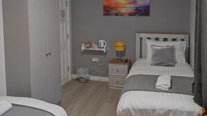 Et hotelværelse med to senge, et billede på væggen, et natbord med en lampe og en lille hylde med genstande.