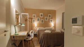 A hotel room with a bed, bedside lamps, a desk with a lamp, a chair, a mirror, and wall art.