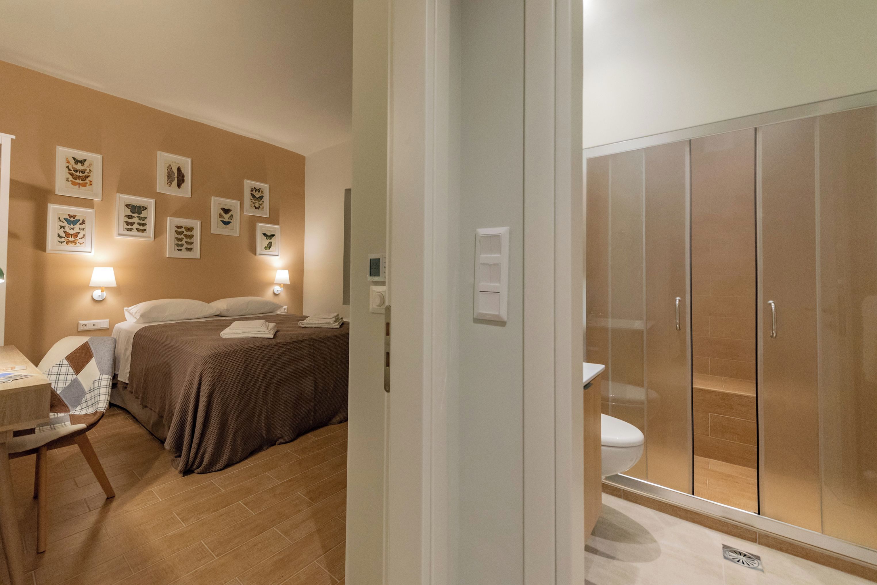 Habitación de hotel con cama, lámparas de noche, escritorio con silla y baño con inodoro y ducha.