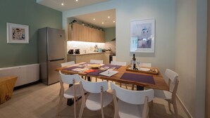 A modern kitchen with wooden cabinets, a stainless steel refrigerator, and a dining area with a wooden table and white chairs.