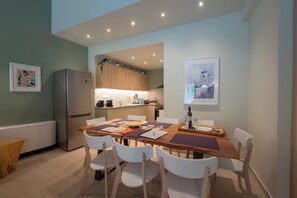 Une cuisine moderne avec des meubles en bois, un réfrigérateur en acier inoxydable et un coin repas comprenant une table en bois et des chaises blanches.