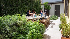 A group of people dining outdoors at a table surrounded by lush greenery and a pathway leading to a building. - Linas Home - Kalamata Mediterranean Villas (Kalamata)