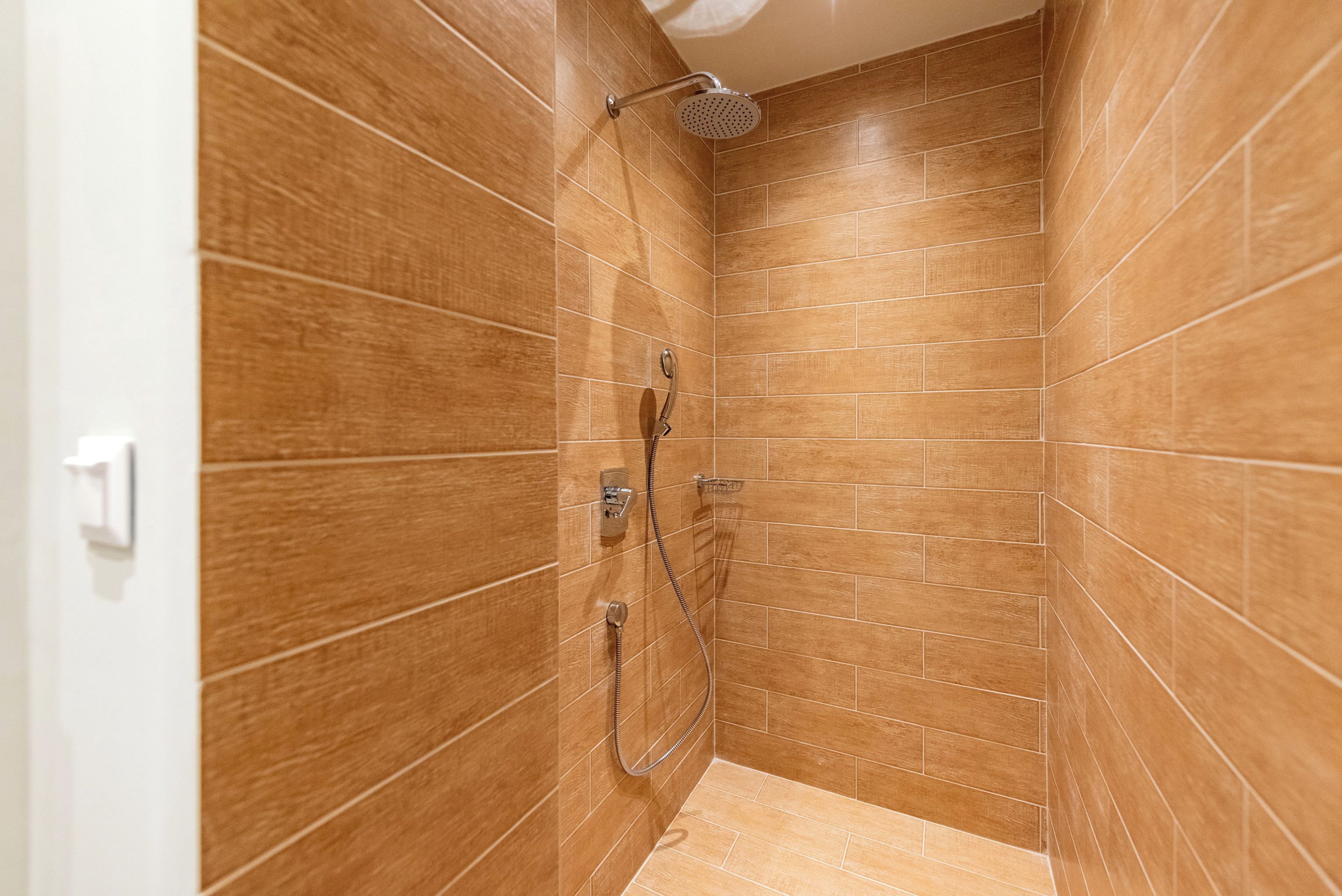Un espace douche avec des carreaux de couleur marron et une pomme de douche à main.