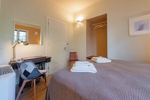 Habitación de hotel con cama, escritorio con silla, espejo, perchero y luz en la pared.