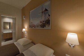 Une chambre d’hôtel avec deux lits, une salle de bain avec un lavabo et un tableau représentant un moulin à vent accroché au mur.