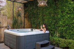 Un bain à remous installé à l’extérieur, entouré d’une clôture en bambou et d’une végétation luxuriante en arrière-plan.