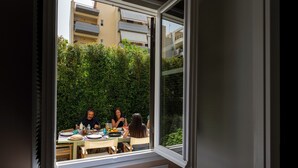 Een kamer met een groot raam met uitzicht op een balkon waar mensen aan het dineren zijn.